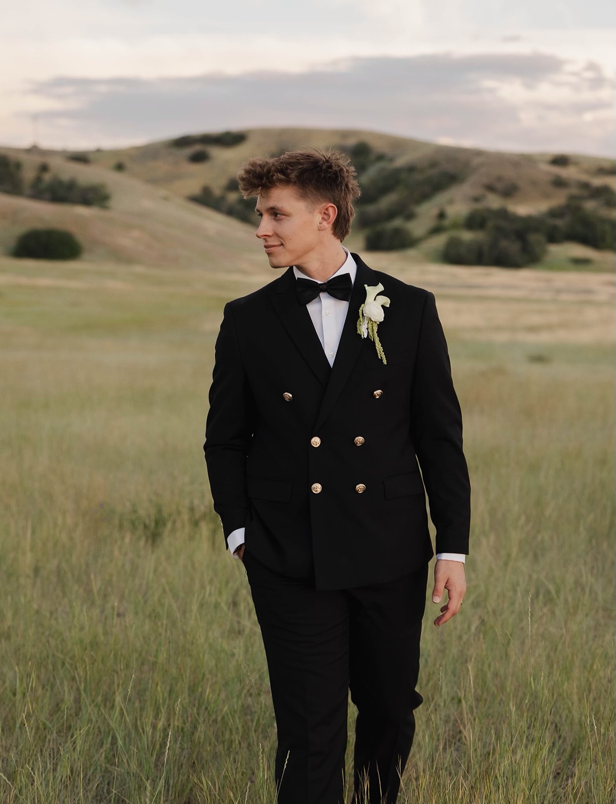 Bodhe Malibu, Utah wedding and event DJ, in a black double-breasted tuxedo in a grassy field